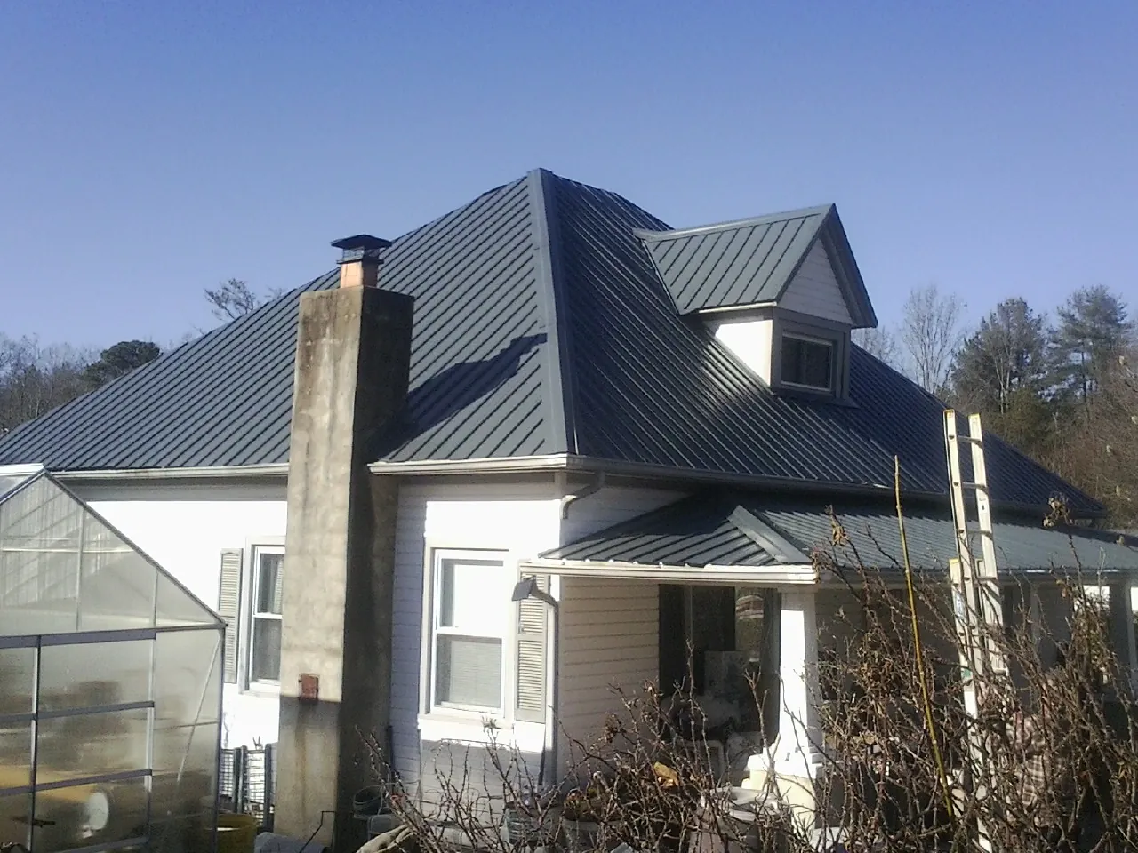 Dark blue standing seam metal roof on a white farmhouse with dormer — Slate & Tile Roof Repair by Roofing Brothers in Pease