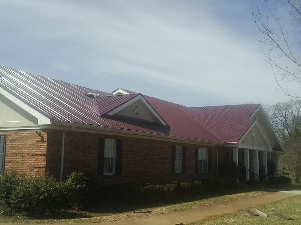 Red metal roof with gabled entries on a long brick building, from a Hail Damage Roof Repair job in Pease
