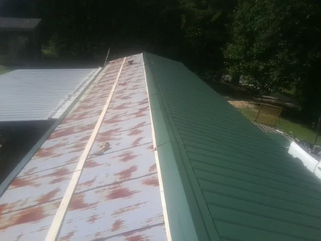 Old rusted panels beside newly installed green metal roofing — Wind Damage Roof Repair by Roofing Brothers in Pease
