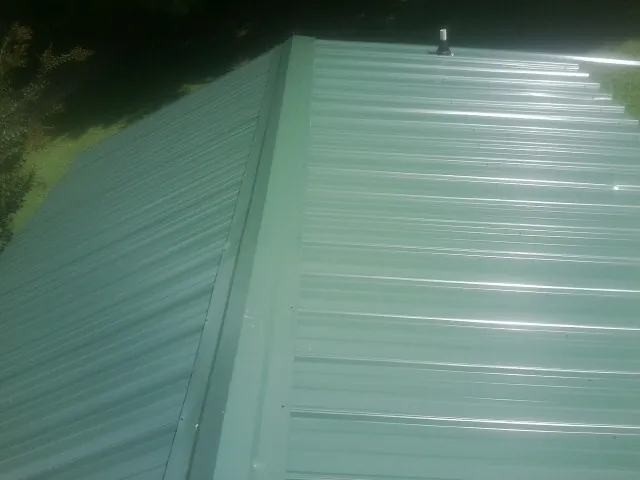 New green metal panels meeting at the ridge of a roof — Flat Roof Repair work by our crew in Pease