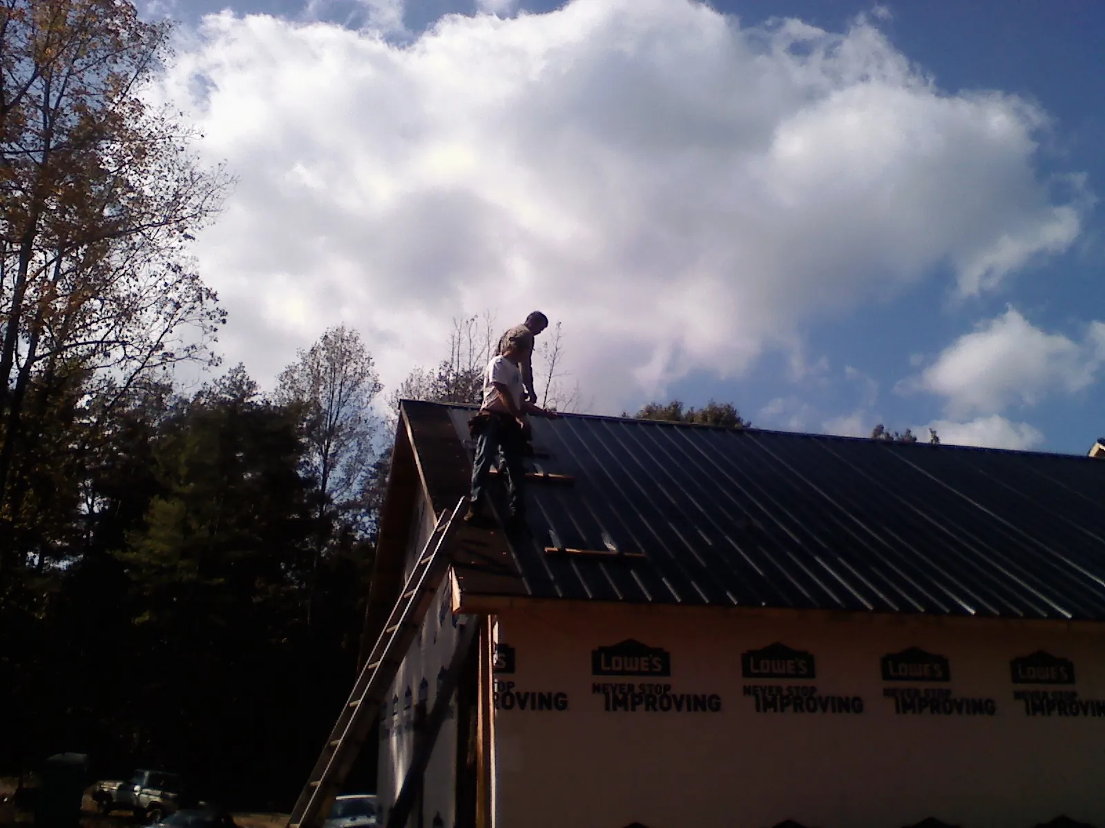 Roofer fastening dark metal panels high against a cloudy sky, from a Roof Inspection job in Pease