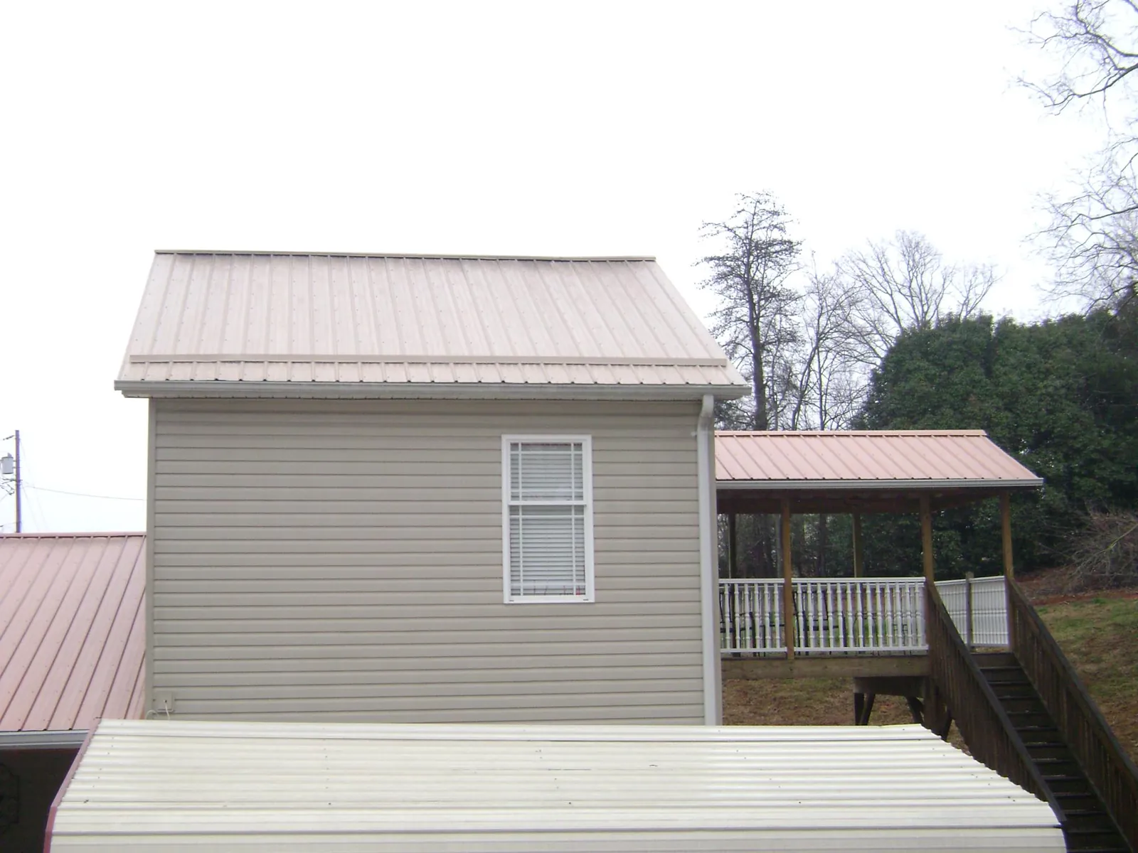 Tan metal roofs on a two story addition and attached porch, from a Roof Replacement job in Pease